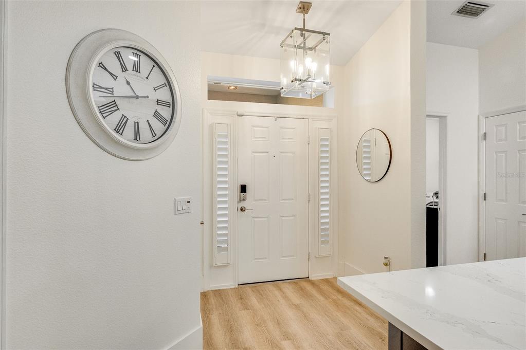 A bright entryway features light wood flooring, a large wall clock, and a modern pendant light — 1373 PAYETTE LANE, WEST MELBOURNE, FL