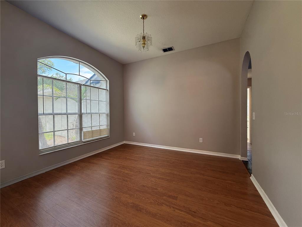 An empty room with wood-look flooring, a large arched window, and a small chandelier — 3510 AUTUMN GLEN DRIVE, VALRICO, FL