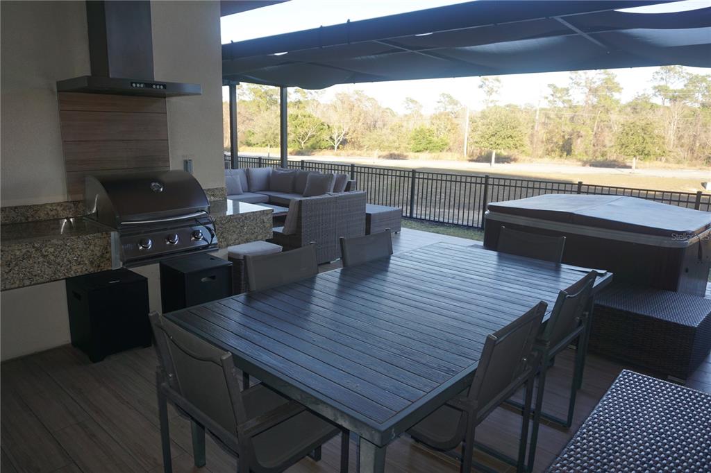 A covered outdoor patio features a dining set, a built-in grill, and a hot tub — 3051 ROCKEFELLER WAY, KISSIMMEE, FL