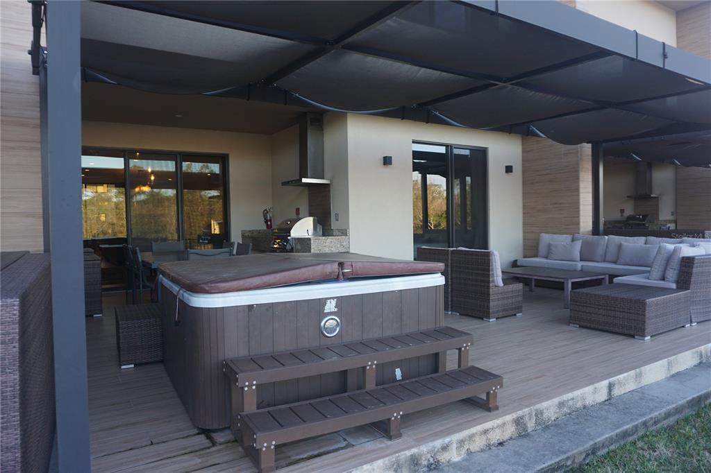 A covered outdoor patio features a hot tub, wicker furniture, and an integrated kitchen area — 3051 ROCKEFELLER WAY, KISSIMMEE, FL