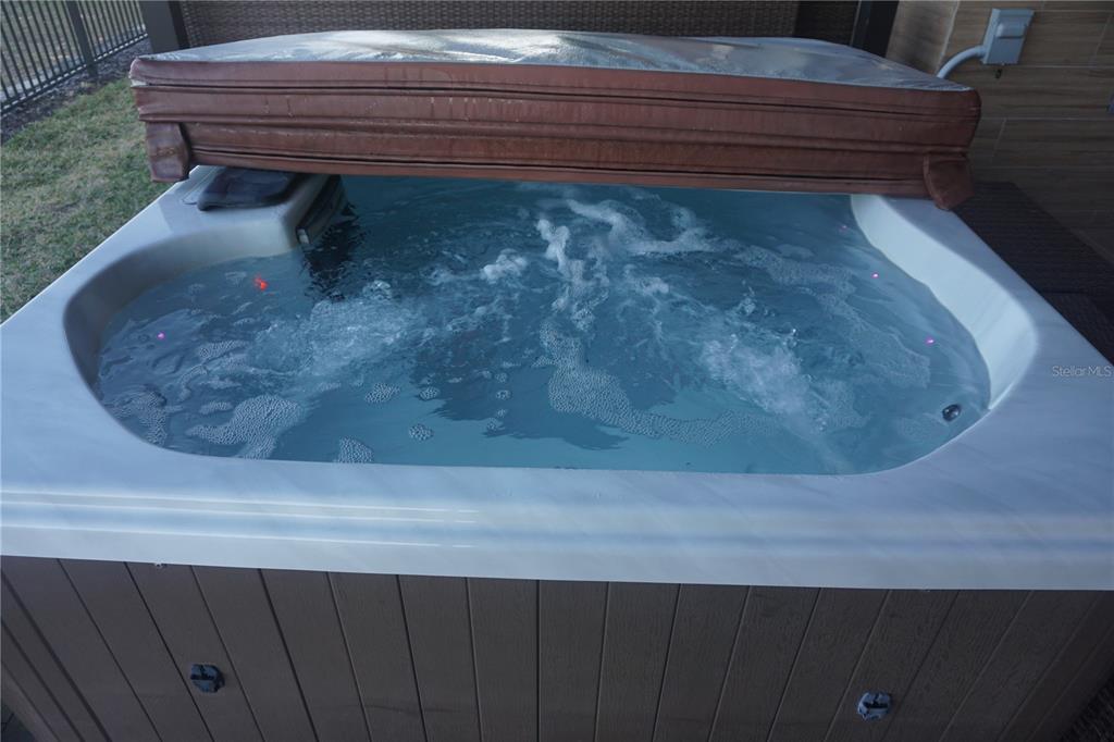 A brown hot tub with an open cover sits on a patio near a fence — 3051 ROCKEFELLER WAY, KISSIMMEE, FL
