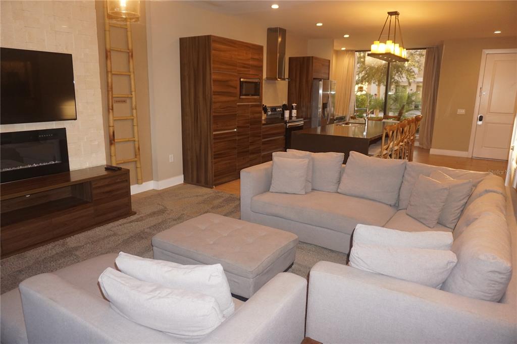 A modern living room features a sectional sofa, fireplace, and an open kitchen with wood cabinetry — 3051 ROCKEFELLER WAY, KISSIMMEE, FL