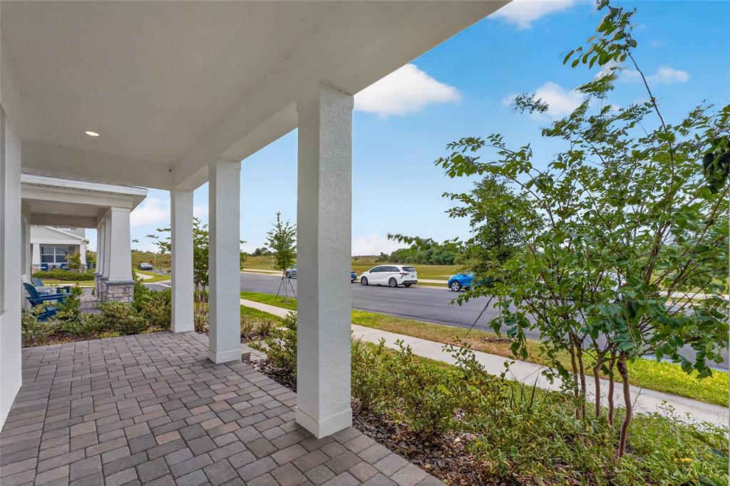 A covered front porch with stone pavers overlooks a suburban street and a small tree — 15174 FIELD DAISY DRIVE, WINTER GARDEN, FL