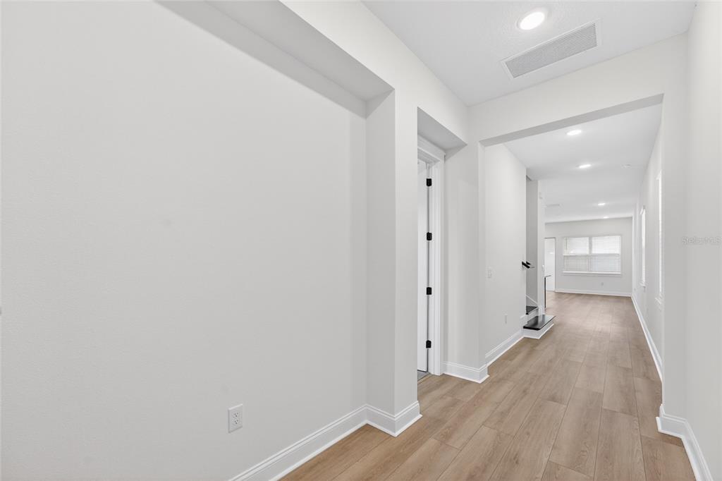 A bright hallway with light wood-look flooring leads toward an open living area — 15174 FIELD DAISY DRIVE, WINTER GARDEN, FL