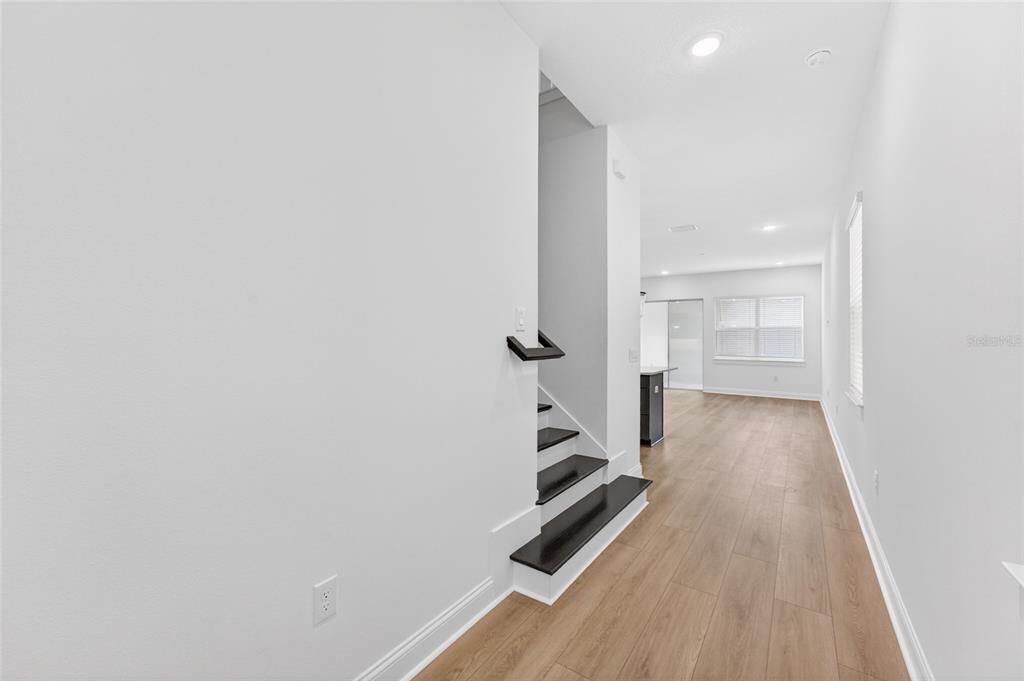 A view of a hallway with wood-look flooring, white walls, and a dark staircase — 15174 FIELD DAISY DRIVE, WINTER GARDEN, FL