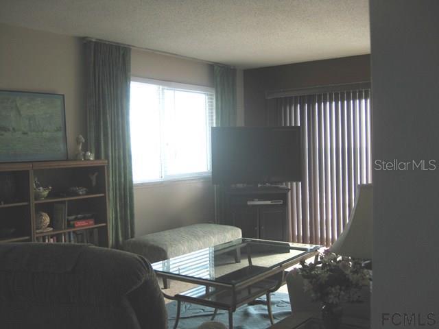 A living room features a glass coffee table, a television on a stand, and window blinds — 3510 S OCEAN SHORE BOULEVARD UNIT 304, FLAGLER BEACH, FL