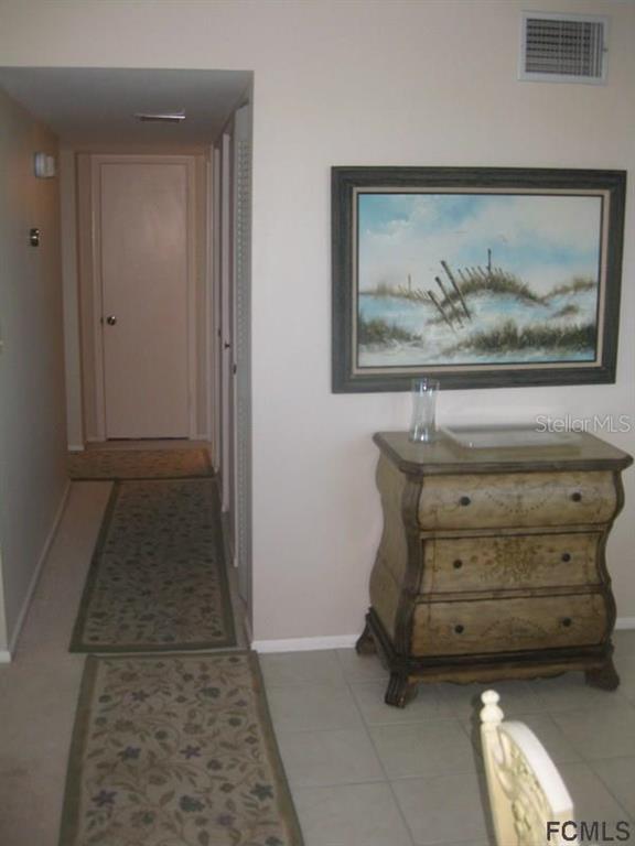 A hallway with a runner rug leads to a closed door beside a small wooden chest — 3510 S OCEAN SHORE BOULEVARD UNIT 304, FLAGLER BEACH, FL