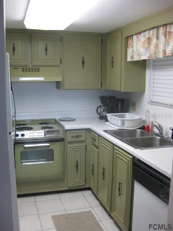 A small kitchen features olive green cabinets, white countertops, a stove, and a double sink — 3510 S OCEAN SHORE BOULEVARD UNIT 304, FLAGLER BEACH, FL