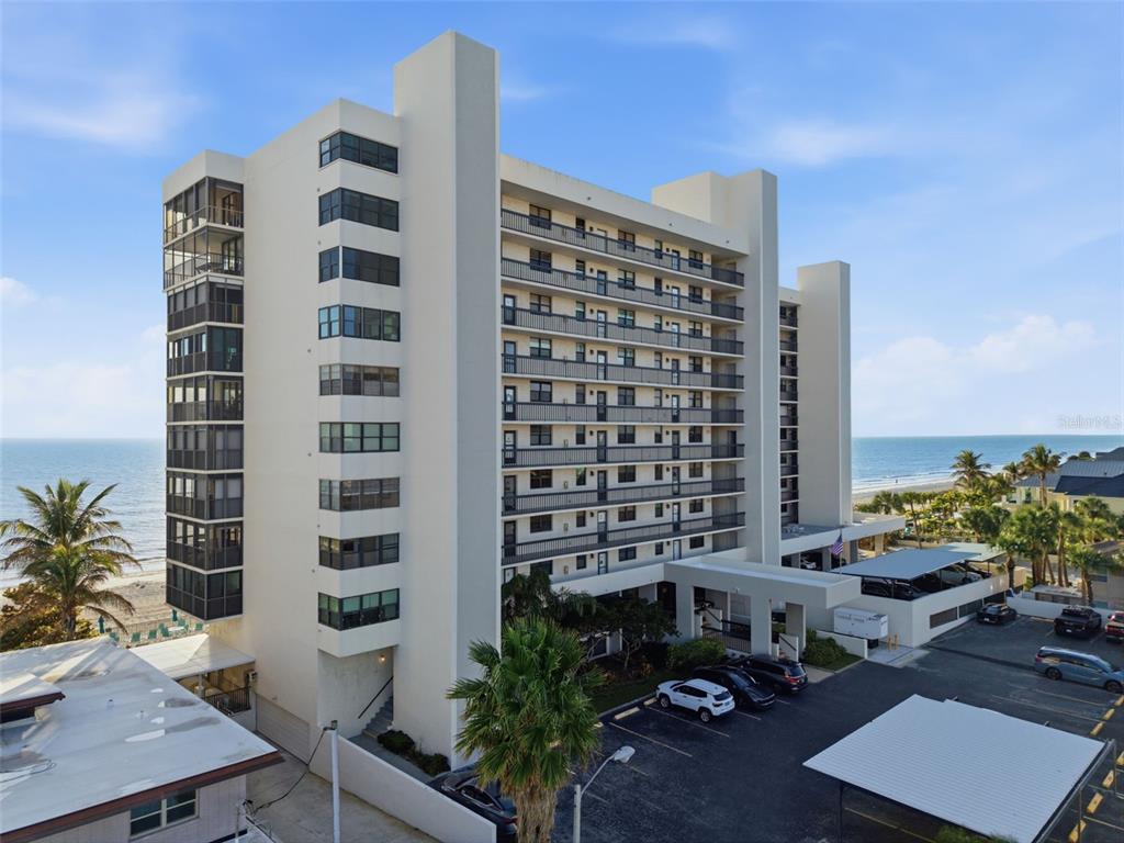 An exterior view of a multi-story beachfront condominium building with parking and palm trees — 15462 GULF BOULEVARD UNIT 406, ST PETERSBURG, FL