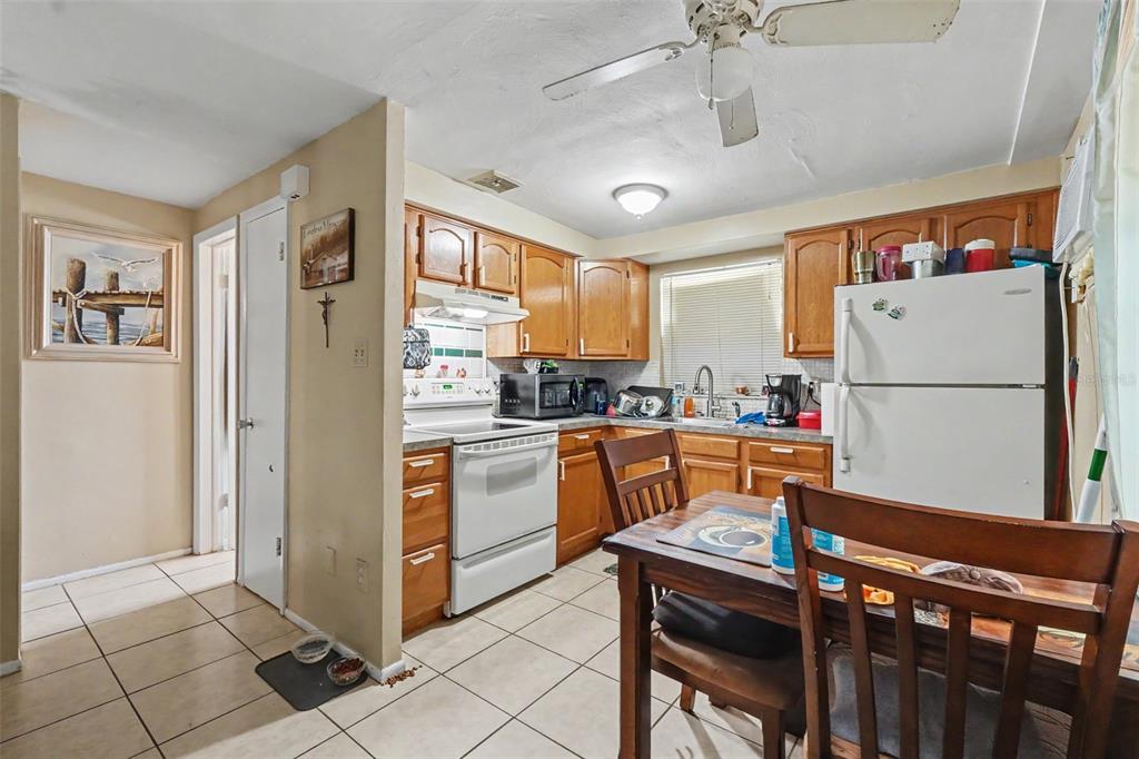 A kitchen with wood cabinets, white appliances, tile flooring, and a small wooden dining table — 5513 OCEANIC ROAD, HOLIDAY, FL