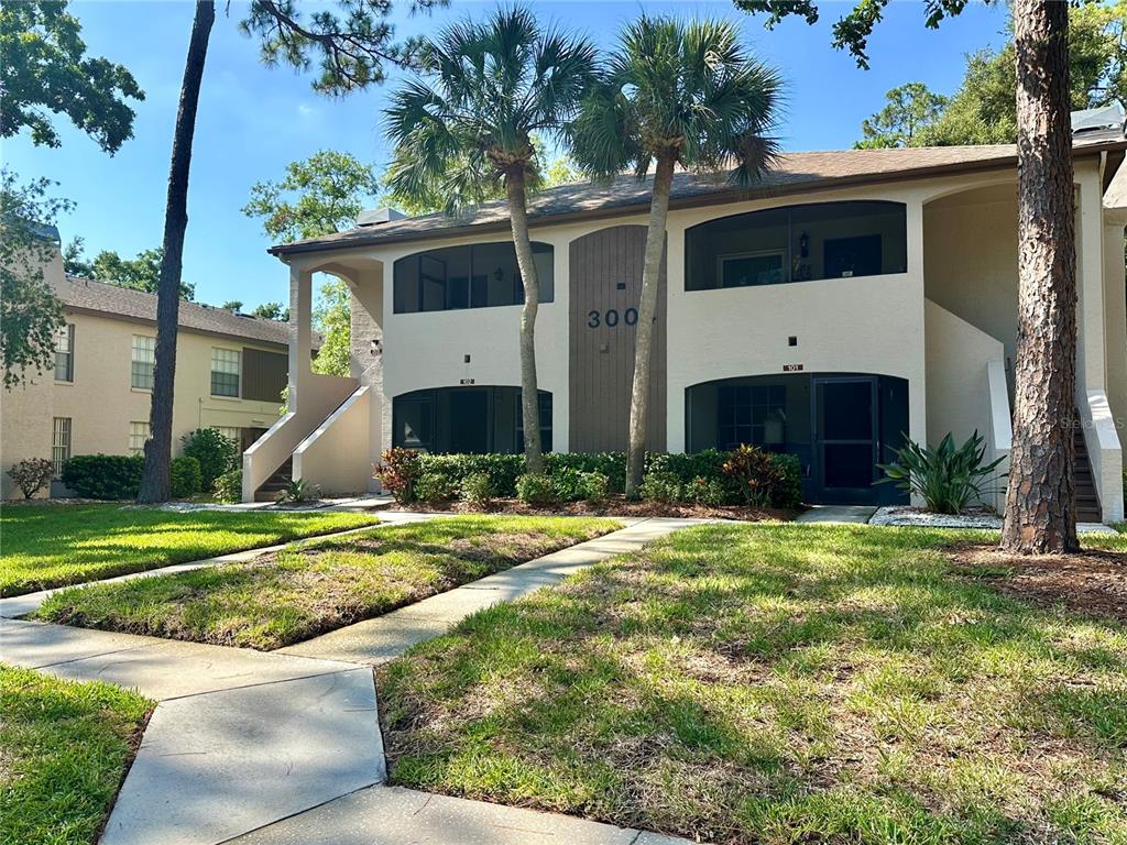 A covered patio features tiled flooring, a brown entry door, and a black wicker loveseat — 3004 BONAVENTURE CIRCLE UNIT 102, PALM HARBOR, FL