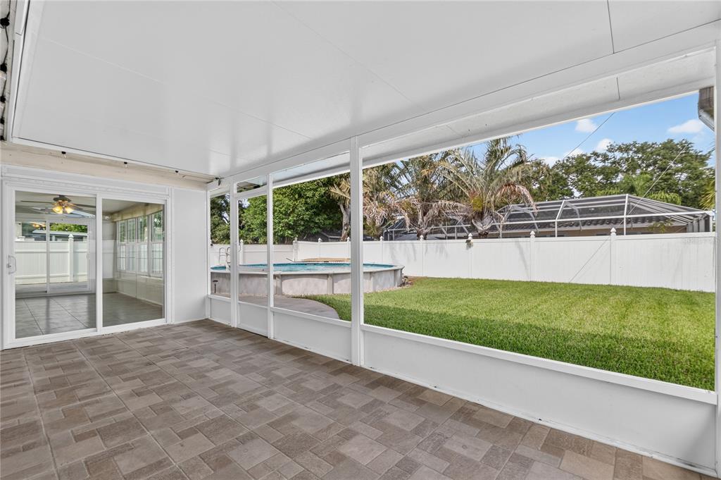 A covered patio with paver flooring overlooks a fenced backyard featuring an above-ground swimming pool — 487 LAKE HILL LANE, LARGO, FL