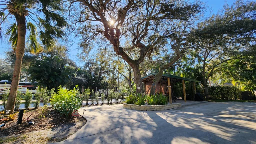 A paved outdoor patio area features a large tree, a covered pavilion, and lush landscaping — 253 SADDLE LANE, RIVER RANCH, FL