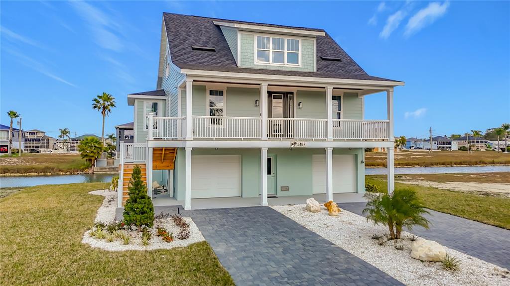 A light green, elevated coastal house features a front porch, garage doors, and a driveway — 3487 SHEEPHEAD DRIVE, HERNANDO BEACH, FL