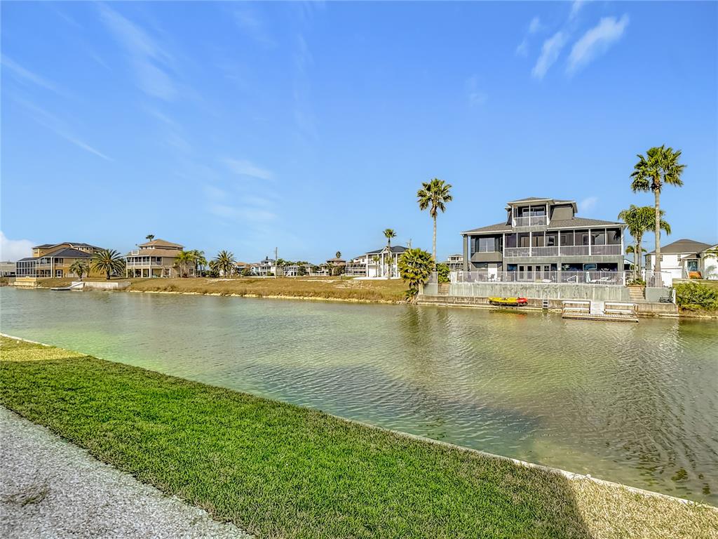 A canal separates a grassy bank from several multi-story houses and palm trees — 3487 SHEEPHEAD DRIVE, HERNANDO BEACH, FL