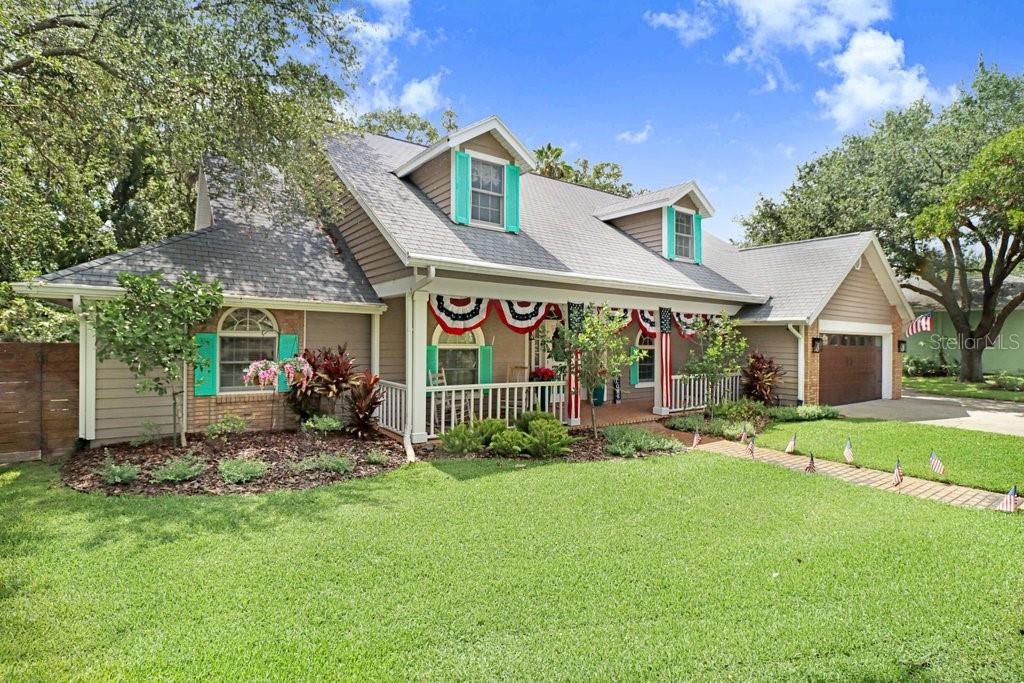 A two-story house with tan siding, a front porch, and teal shutters on a sunny day — 1976 DUNLOE CIRCLE, DUNEDIN, FL