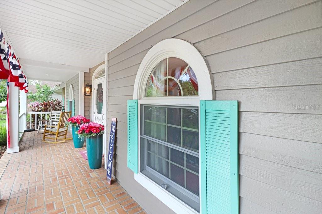 A covered brick porch features a window with teal shutters and a welcome sign — 1976 DUNLOE CIRCLE, DUNEDIN, FL
