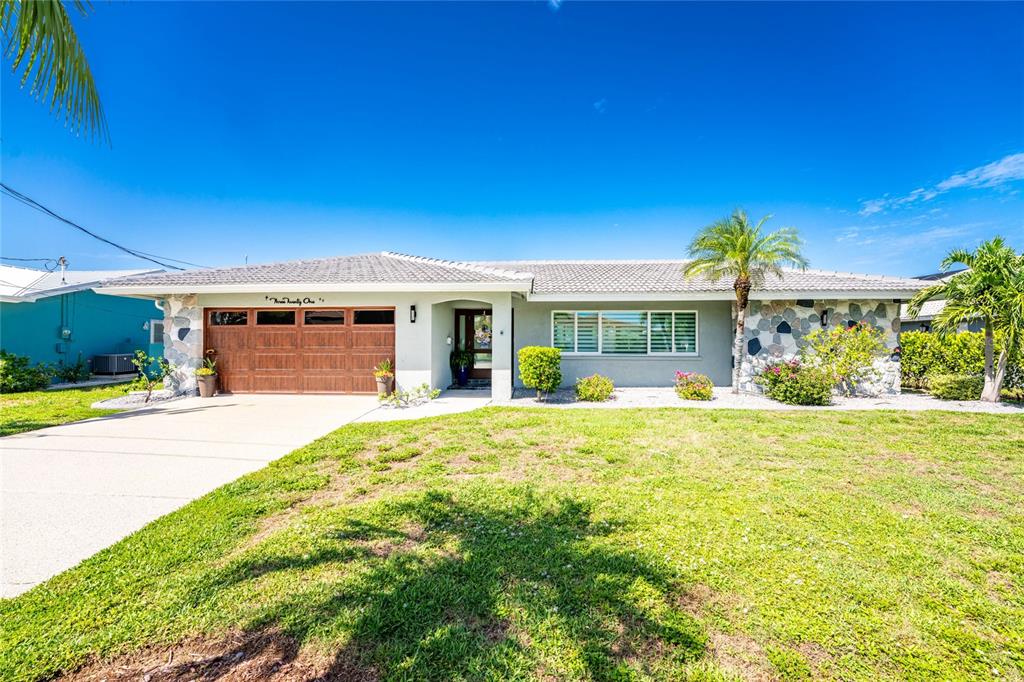 A single-story house with a stone facade, a wooden garage door, and a palm tree — 321 CAPRI ISLES CT, PUNTA GORDA, FL