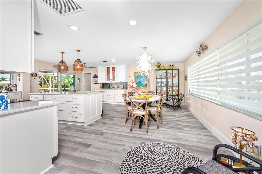 A bright, open-concept kitchen and dining area features white cabinetry, wood-look flooring, and pendant lighting — 321 CAPRI ISLES CT, PUNTA GORDA, FL
