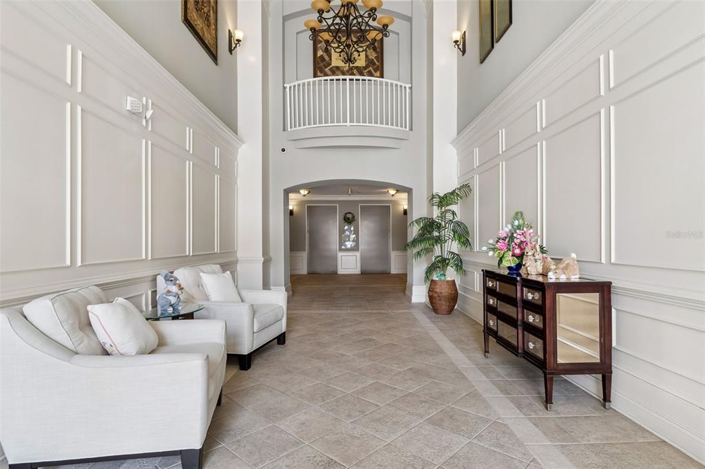 A formal lobby features white paneled walls, two armchairs, a mirrored console table, and elevators — 7903 SEMINOLE BOULEVARD UNIT 2208, SEMINOLE, FL