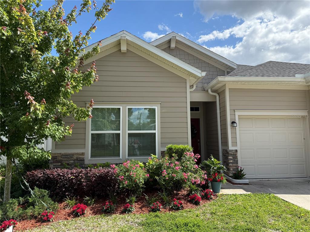A single-story house exterior features tan siding, a stone base, and a front-facing garage — 7656 SW 74TH LOOP, OCALA, FL