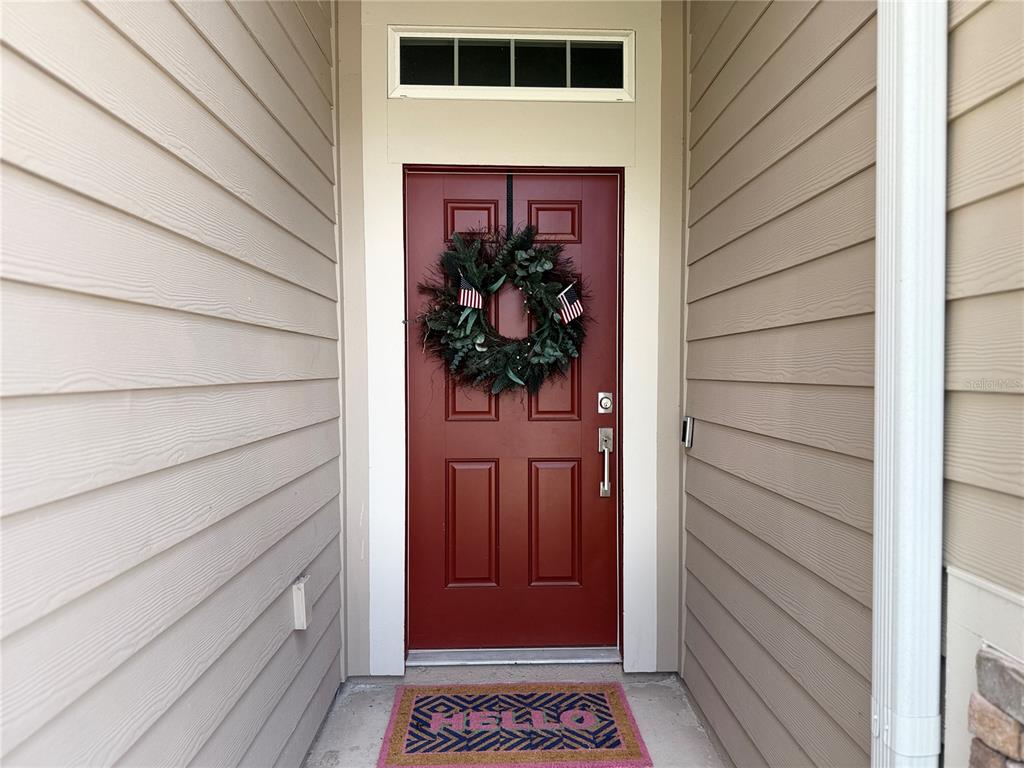 A red front door with a wreath and a welcome mat sits between beige siding — 7656 SW 74TH LOOP, OCALA, FL