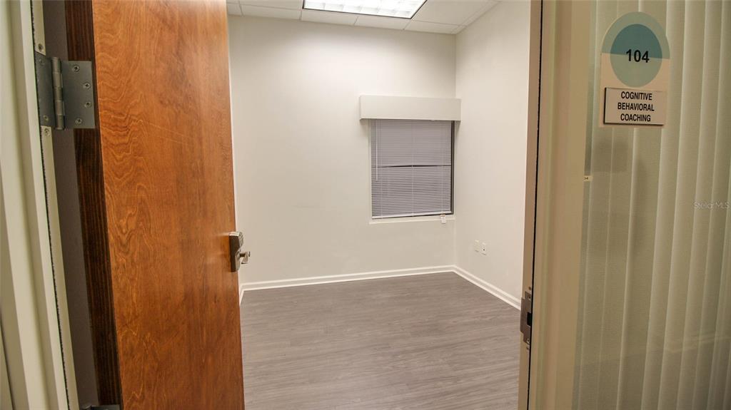 An empty office room features light-colored walls, gray wood-look flooring, and a single window — 8865 COMMODITY CIRCLE UNIT 106, ORLANDO, FL