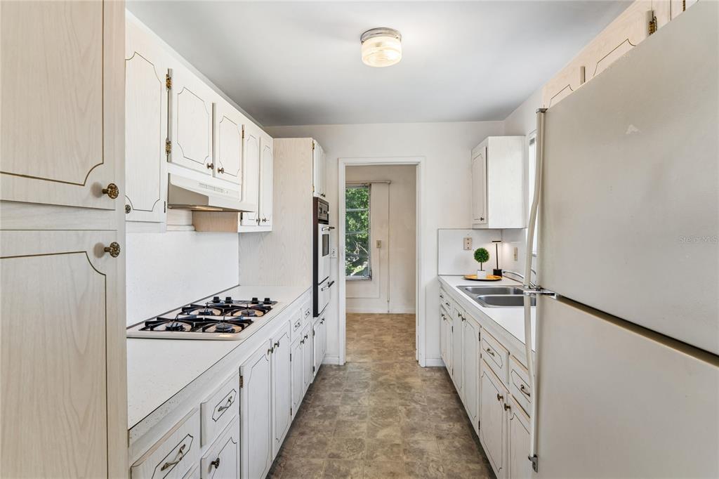 A galley kitchen features white cabinets, a gas cooktop, a double sink, and vinyl flooring — 5530 N 80TH STREET UNIT C308, ST PETERSBURG, FL