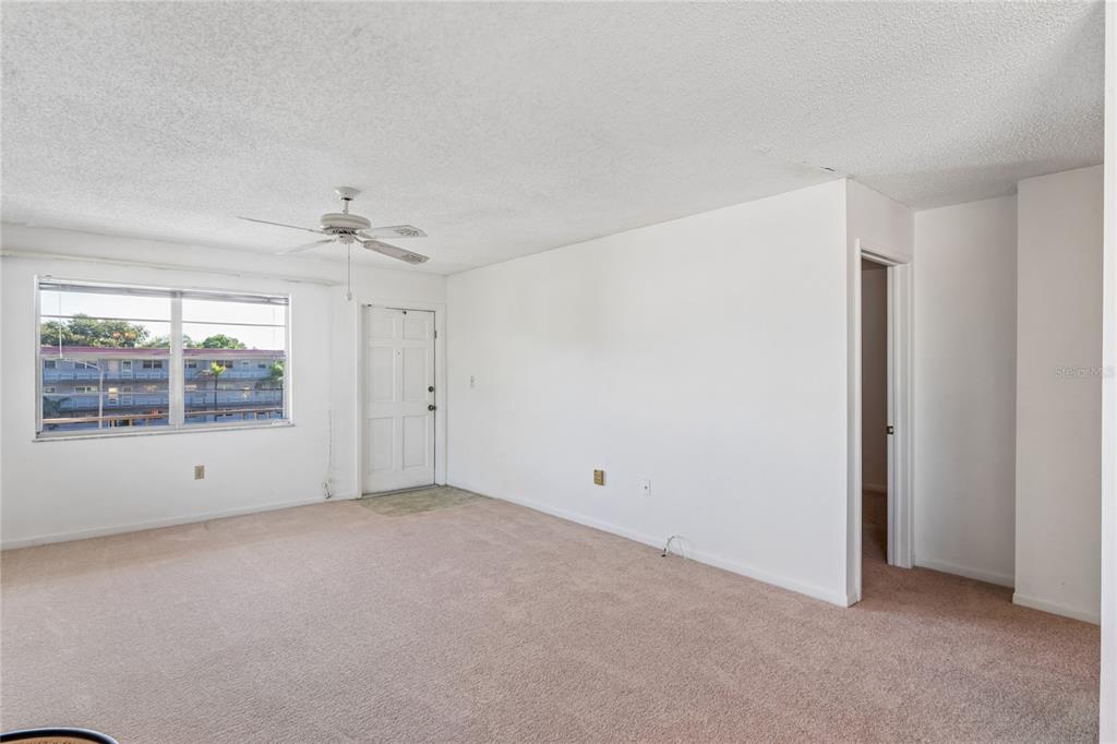 An empty living room features beige carpet, white walls, a ceiling fan, and a front door — 5530 N 80TH STREET UNIT C308, ST PETERSBURG, FL