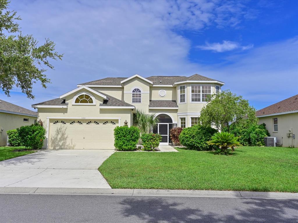 A two-story suburban house with a beige stucco exterior, a two-car garage, and a lawn — 5184 51ST LANE W, BRADENTON, FL