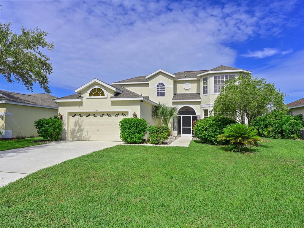 A two-story suburban house with a beige stucco exterior, a two-car garage, and green lawn — 5184 51ST LANE W, BRADENTON, FL