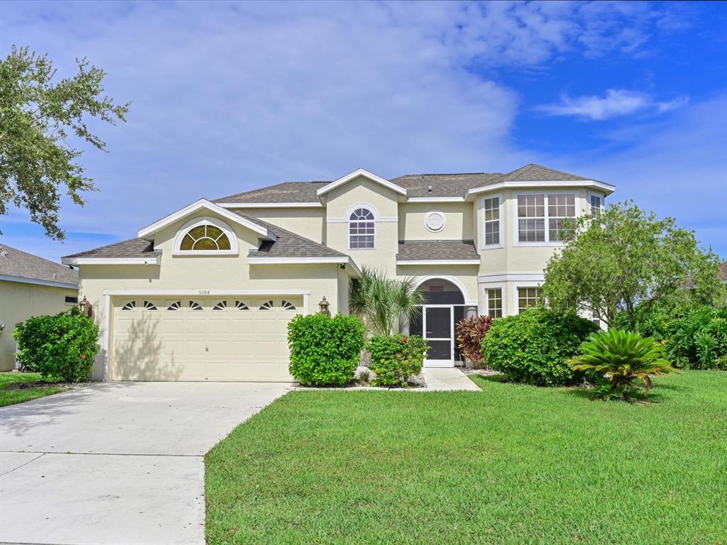 A two-story suburban house with a beige stucco exterior, a two-car garage, and green landscaping — 5184 51ST LANE W, BRADENTON, FL