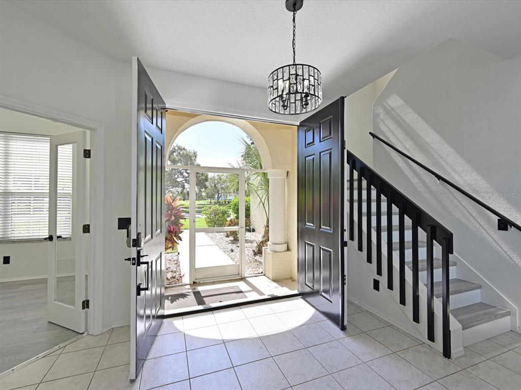 An entryway features a tiled floor, a black chandelier, and a staircase with black railings — 5184 51ST LANE W, BRADENTON, FL