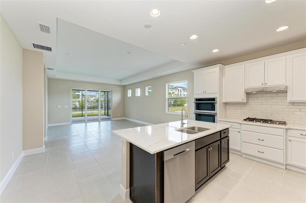 A modern kitchen with a dark island, white cabinets, and an adjacent open living area — 149 OKEEFFE CIRCLE, BRADENTON, FL