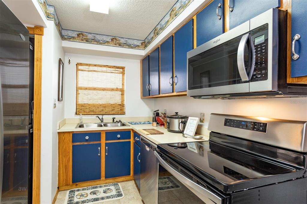 A kitchen features blue cabinets with wood trim, stainless steel appliances, and a window with blinds — 3170 OCEAN SHORE BOULEVARD UNIT 305, ORMOND BEACH, FL