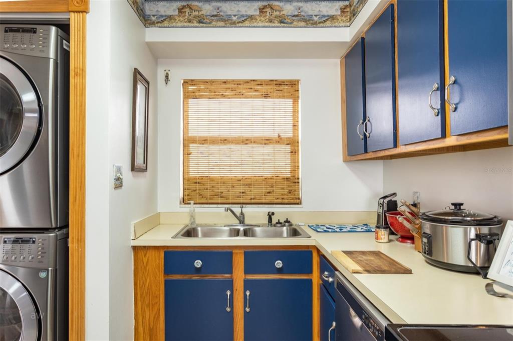 A kitchen features blue cabinets, a double sink, a window with bamboo blinds, and appliances — 3170 OCEAN SHORE BOULEVARD UNIT 305, ORMOND BEACH, FL