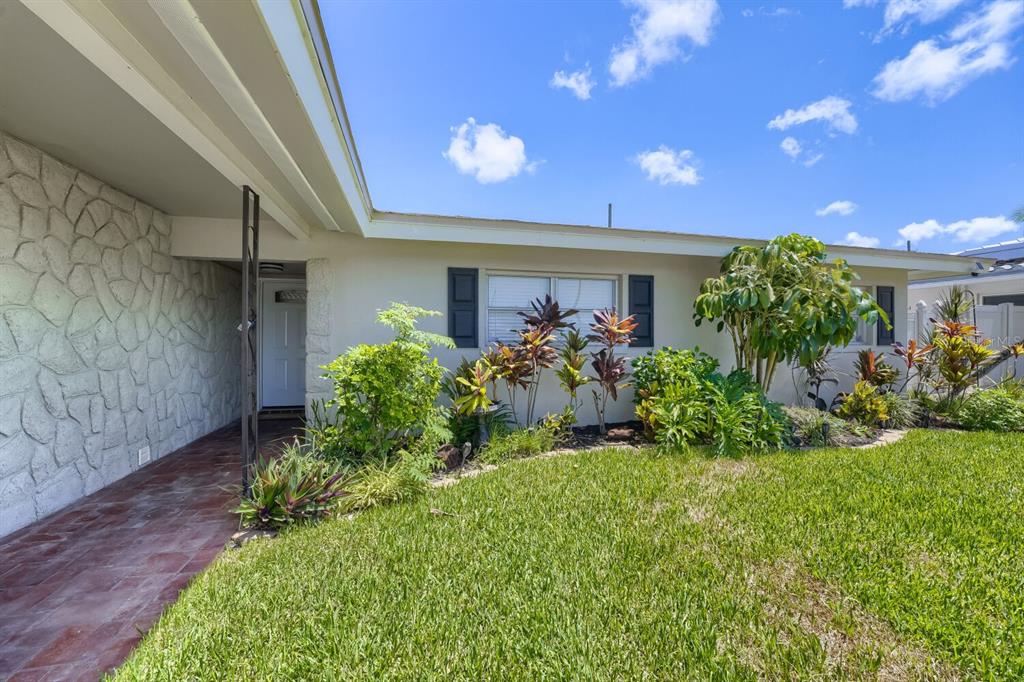 The exterior of a house features a stone-clad wall, a tiled walkway, and landscaped garden beds — 13931 DOMINICA DRIVE, SEMINOLE, FL