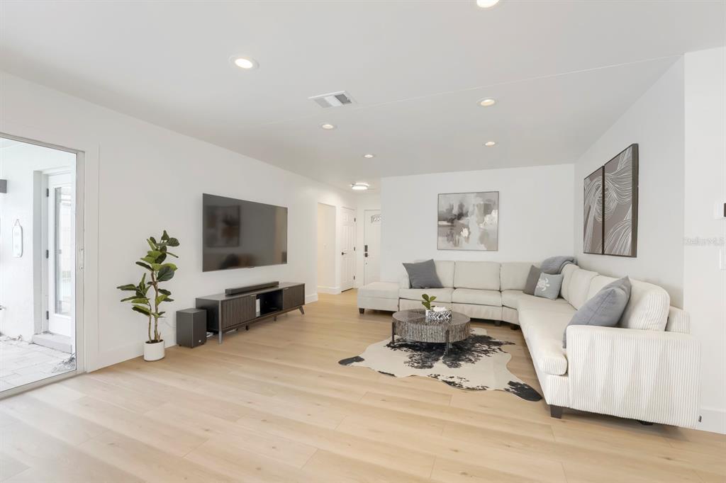 A bright living room features light wood floors, a large sectional sofa, and a wall-mounted television — 13931 DOMINICA DRIVE, SEMINOLE, FL