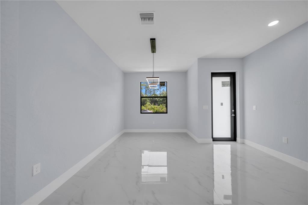 A bright dining room features white walls, glossy marble-look tile flooring, and a modern pendant light — 1009 MOORE AVENUE, LEHIGH ACRES, FL