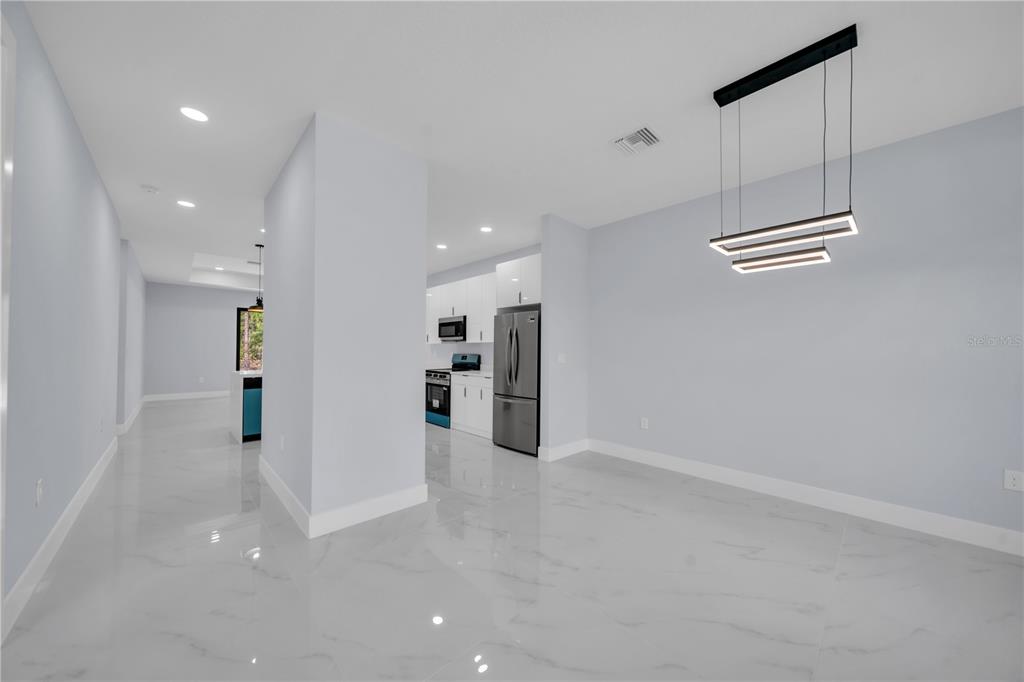 A modern kitchen and dining area feature white cabinetry, stainless steel appliances, and marble-look flooring — 1009 MOORE AVENUE, LEHIGH ACRES, FL