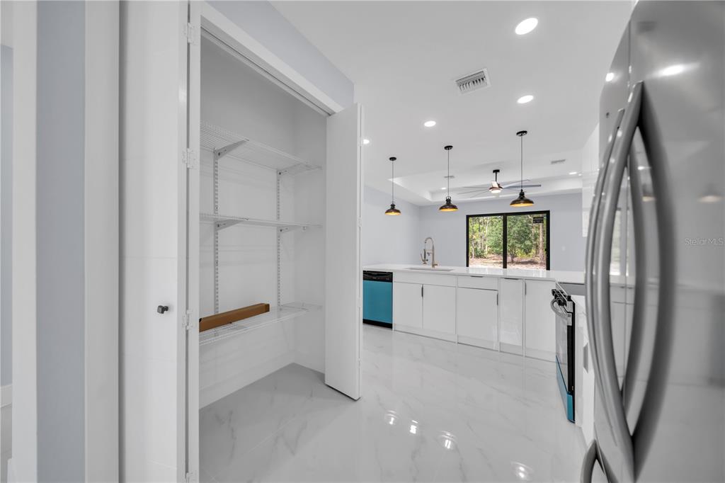 A white kitchen features a walk-in pantry, stainless steel appliances, and light-colored tile flooring — 1009 MOORE AVENUE, LEHIGH ACRES, FL