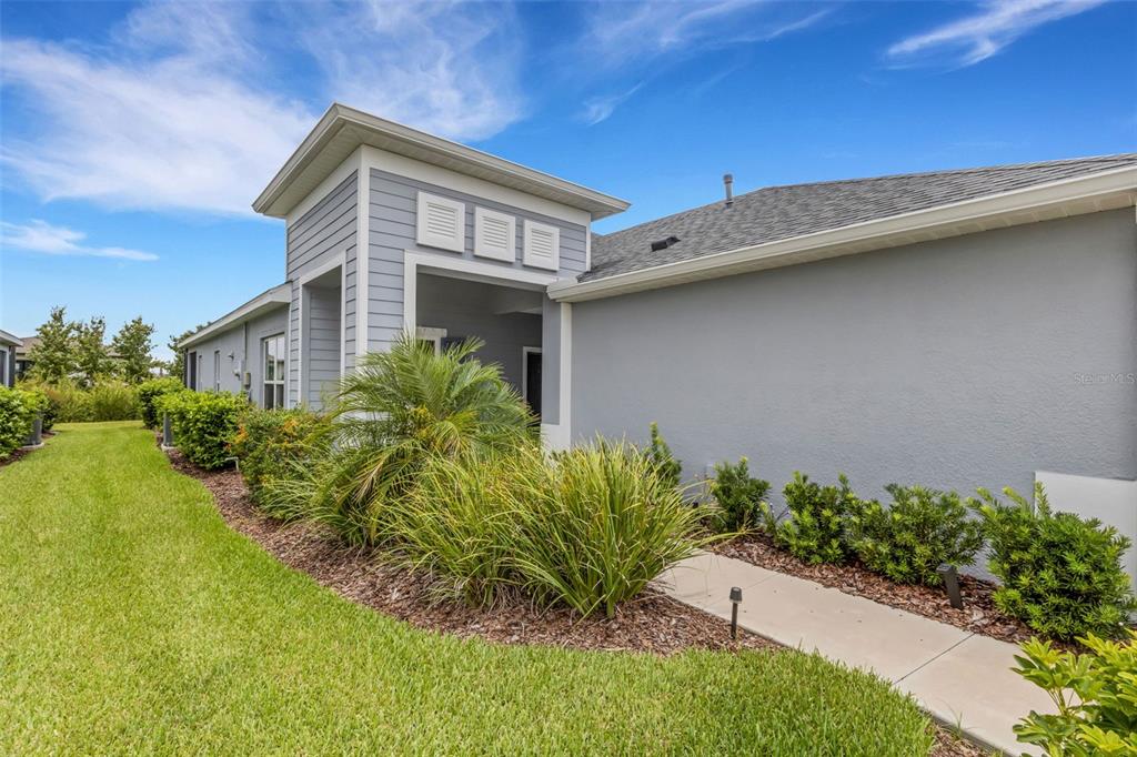 A side view of a gray house with a covered entryway and landscaped lawn — 4657 WILLOW BEND AVENUE, PARRISH, FL