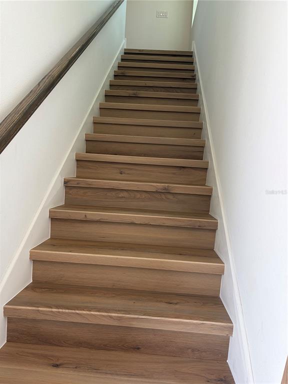 A straight staircase features wooden treads and white walls with a dark handrail — 2984 EMBARK TRAIL, ST CLOUD, FL