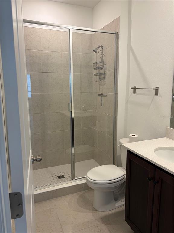 A bathroom features a tiled walk-in shower, a toilet, and a dark wood vanity — 2984 EMBARK TRAIL, ST CLOUD, FL