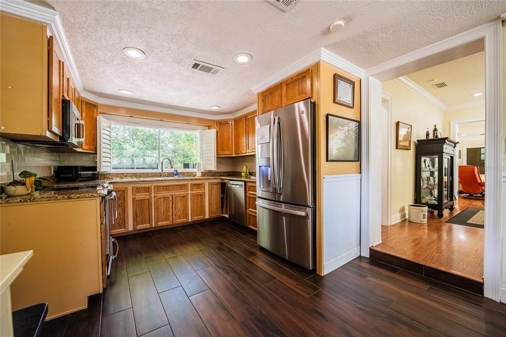 A kitchen with wood cabinets, stainless steel appliances, granite countertops, and dark wood-look tile flooring — 2804 NEVADA ROAD, LAKELAND, FL