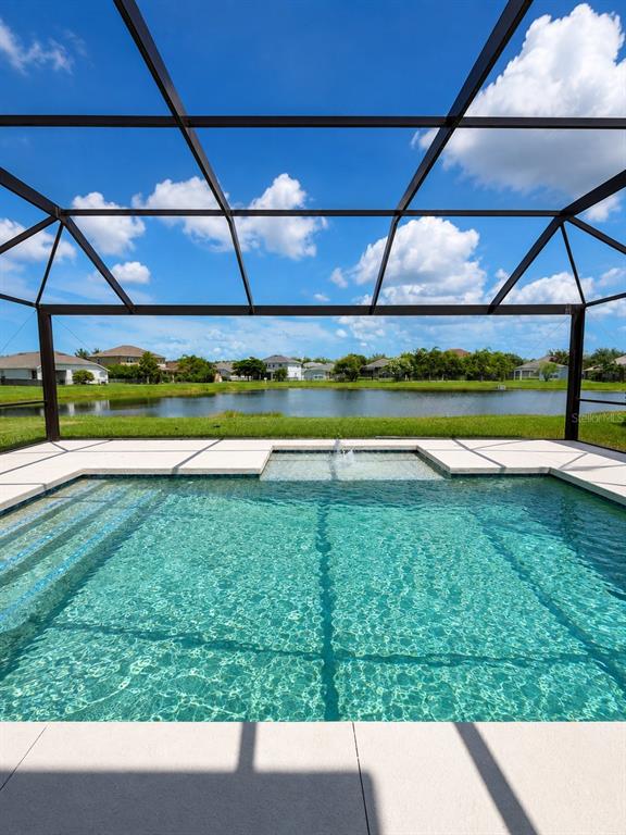 A swimming pool with a fountain and a screened enclosure overlooks a lake and houses — 9950 58TH STREET E, PARRISH, FL