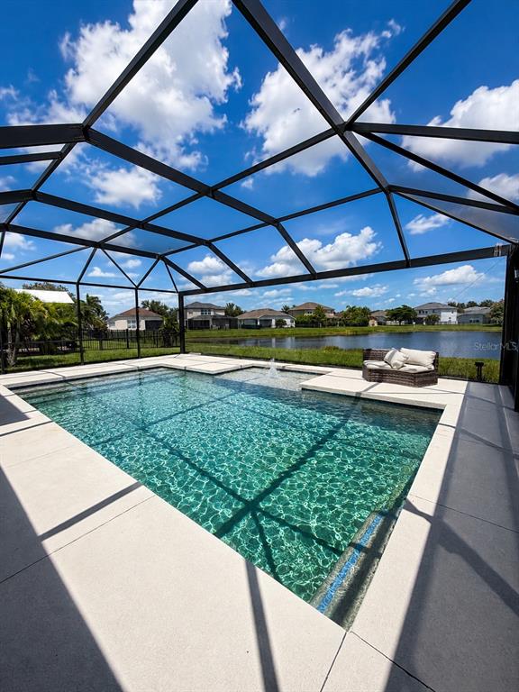 A screened-in swimming pool with a fountain overlooks a lake and neighboring houses — 9950 58TH STREET E, PARRISH, FL