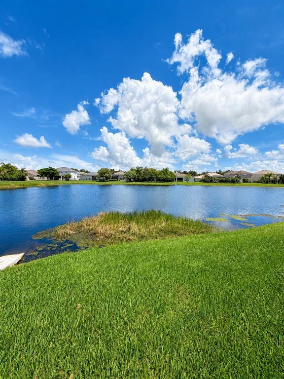 A grassy lawn overlooks a pond with houses in the background under a blue sky — 9950 58TH STREET E, PARRISH, FL