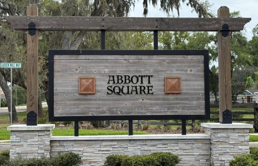 A wooden sign for Abbott Square stands on a stone base with a street sign nearby — 36347 CAMP FIRE TERRACE, ZEPHYRHILLS, FL