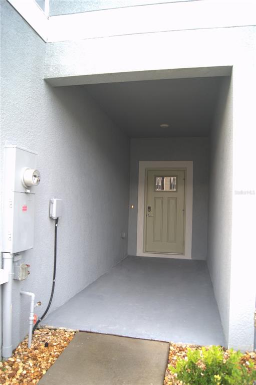 A recessed entryway features a light-colored door, gray painted floor, and an exterior utility meter — 36347 CAMP FIRE TERRACE, ZEPHYRHILLS, FL